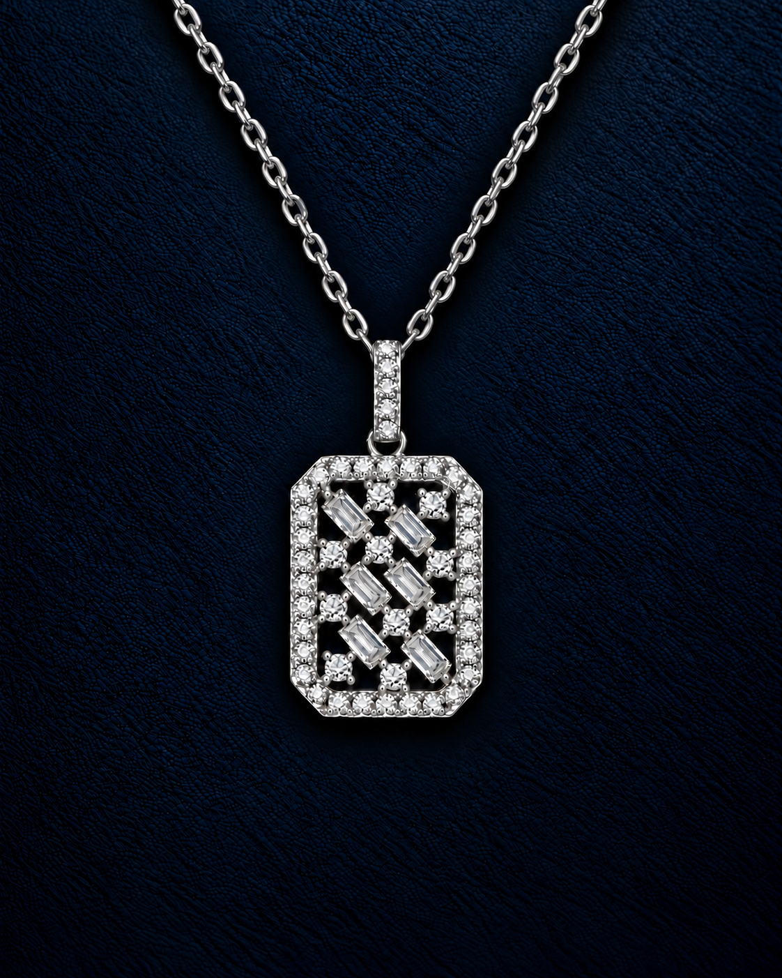 Solene pendant, a rectangular silver pendant with a crisscross lattice of baguette and round stones inside a stone-set frame, hanging from a fine cable chain against dark navy leather.